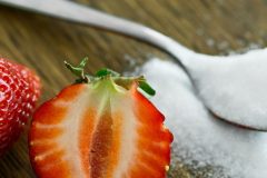 a strawberry halved in the foreground and a teaspoon of sugar in background